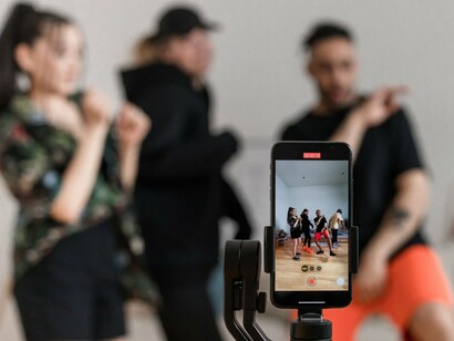 People dancing while being recorded on a smartphone, reflecting the culture of sharing ordinary moments online