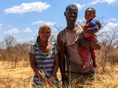 An African family stands in a drought-stricken field, reflecting the challenges faced by communities affected by poverty and environmental hardshi