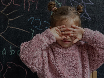A young girl exhibiting signs of dysregulation stands in front of a blackboard in a classroom setting