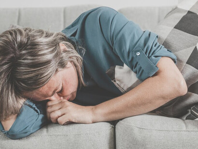 Adult woman crying on the couch at home, expressing loss, grief, death, mourning, sadness, and sorrow