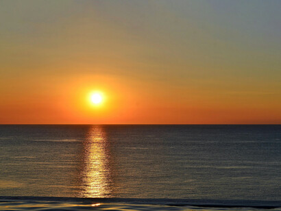 A sunrise over the sea, creating an orange trail over the waves