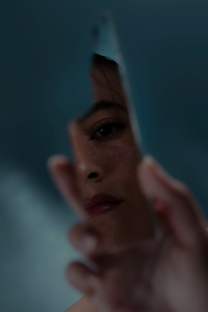 A mysterious woman gazes into a shattered mirror, capturing a moment of introspection and fragments of reflection