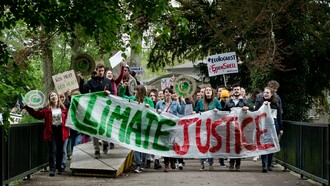 A group of activists marches through the streets carrying banners and signs demanding climate justice during a public demonstration in Maastricht, LI, Netherlands
