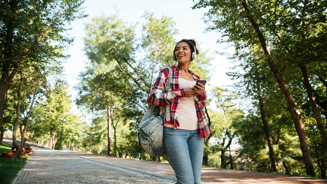 A young woman enjoying a walk, listening to music and smiling at her surroundings