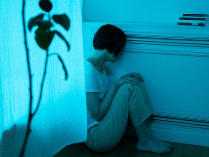 A woman sitting in the corner of her room depressed