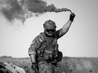 A soldier signals with a smoke flare amidst a desolate battlefield, highlighting the human cost of global conflicts and the shifting dynamics of international order