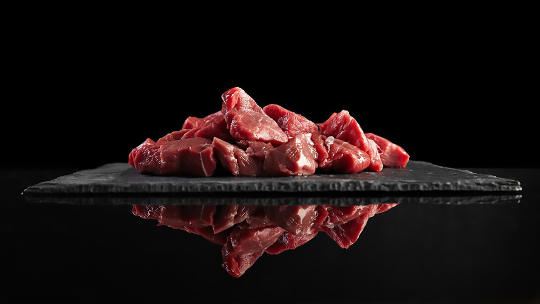 Pieces of raw, fresh meat displayed on a black stone board, beautifully mirrored for a striking presentation