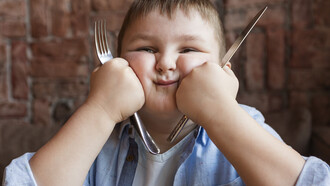 An obese boy holding cutlery, ready to eat