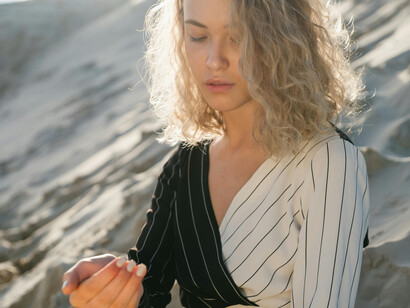 A woman with curly blonde hair in the desert, holding her hand up, looking down