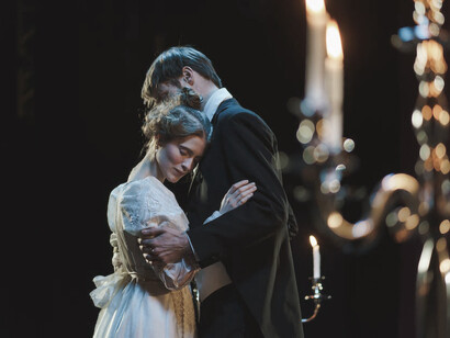 A man and a woman, standing in close proximity to each other on a theater stage
