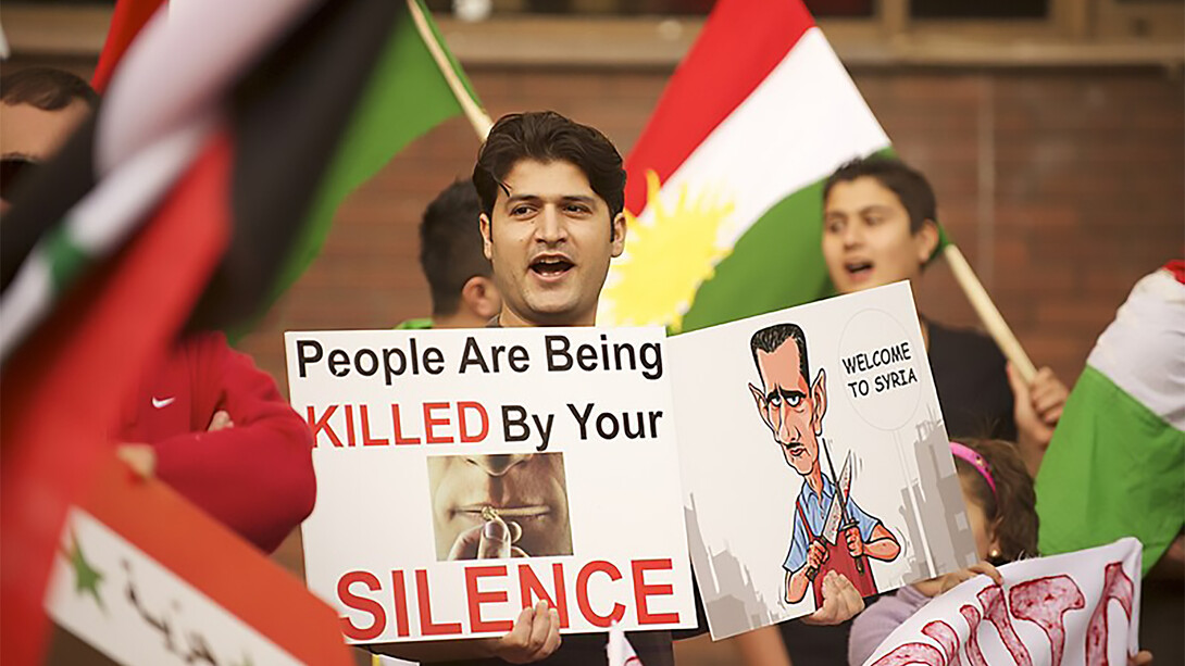 A man participating in the Syrian protests holds a sign that reads: "People are being killed by your silence"
