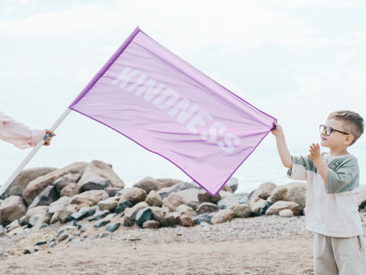 A boy on the beach holding a kindness flag in the wind