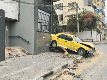 A yellow car is parked on the roadside amidst scenes of devastation in Gaza, following the bombing by the State of Israel that began on October 7, 2023