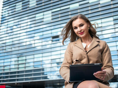 A businesswoman using a digital tablet outside a modern office building, symbolizing women's economic empowerment and the intersection of feminism