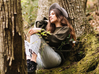 A young woman, immersed in nature, sits on a tree with a camera, capturing the tranquility of stillness and mindfulness during peaceful moments