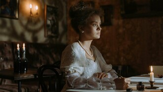 A woman seated in dim candlelight with pen in hand, representing the psychological aftermath of the Spanish flu