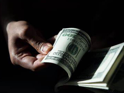 A person’s hand grips several dollar bills, the crisp notes fanned out visibly