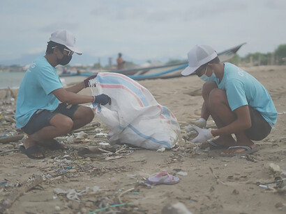 Two Indonesian men are diligently cleaning the beach on behalf of an ocean cleanup organization