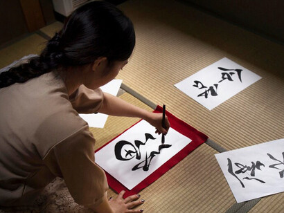 A woman gracefully practicing Japanese calligraphy, creating kanji characters that reflect the wisdom of Oubaitori, the philosophy of blooming in one's own time