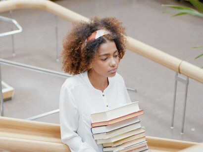 Holding a stack of books, this student stands as a symbol of the university's role in transitioning from outdated research methods to a more creative and effective approach