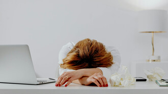 A female writer resting her head on the table beside a laptop, looking anxious and depressed