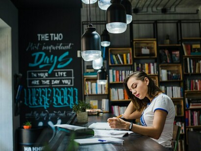 A young woman studying intently at a table, surrounded by notebooks, demonstrating strong focus and motivation