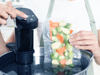The concerning reality of plastic consumption as a woman places vacuum-sealed food into a pot with a sous vide cooker, emphasizing the adverse effects of plastic dependency in kitchen activities
