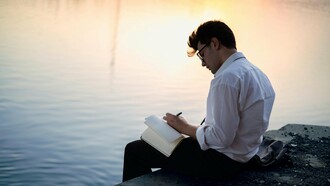 À beira de um lago ou mar tranquilo, um homem registra ideias em seu caderno enquanto a luz dourada envolve a cena. Longe da pressão e das regras, o pensamento volta a fluir com naturalidade
