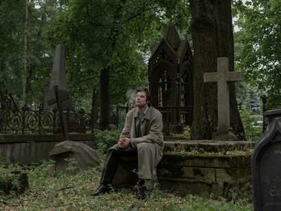 A man sitting near a tombstone while smoking his cigarette and reflecting on his grief