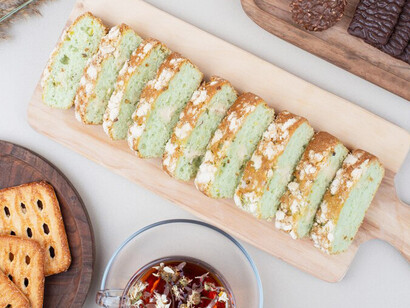 Indulge in a delightful afternoon break with slices of zucchini cake, biscuits, and a steaming cup of tea, presented elegantly on a serene white surface