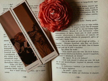 A crimson rose on a book, next to a bookmark with a flowery design