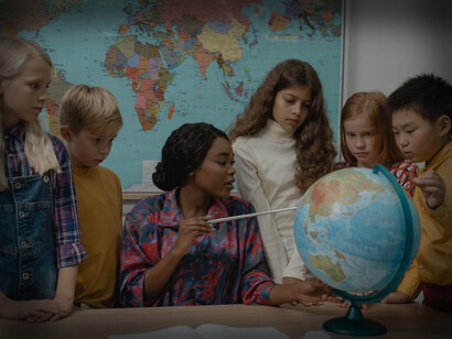 A female teacher is showing the countries on the globe to five students