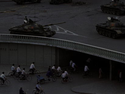 June 6, 1989, file photo, bicycling commuters pass through a tunnel as above on Beijing's Jianguomenwai overpass military tanks are positioned, two days after the Tiananmen Square massacre, AP Photo/Vincent Yu via the Nation