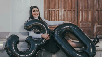 A woman sitting on the floor with balloons, celebrating her 30th birthday