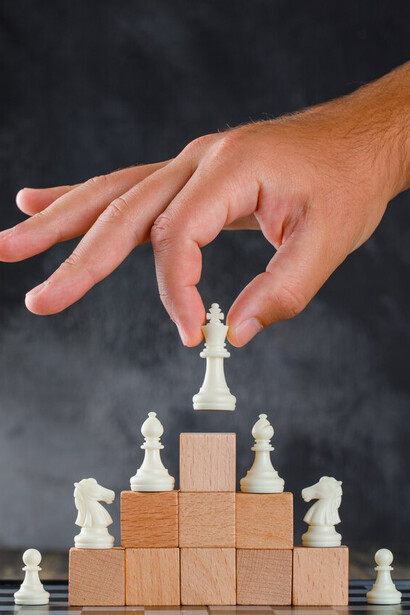 Strategic business success: a man positioning a chess piece on a pyramid of blocks, representing calculated moves toward achieving goals