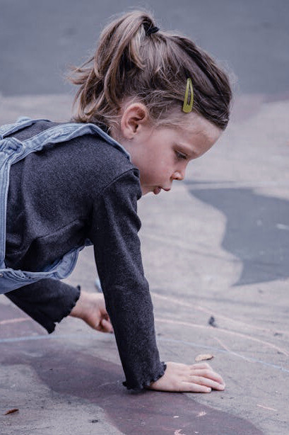 Drawing her hopscotch grid with focused precision, the young girl channels the spirit of generations before her, creating a playground canvas for endless joy and camaraderie