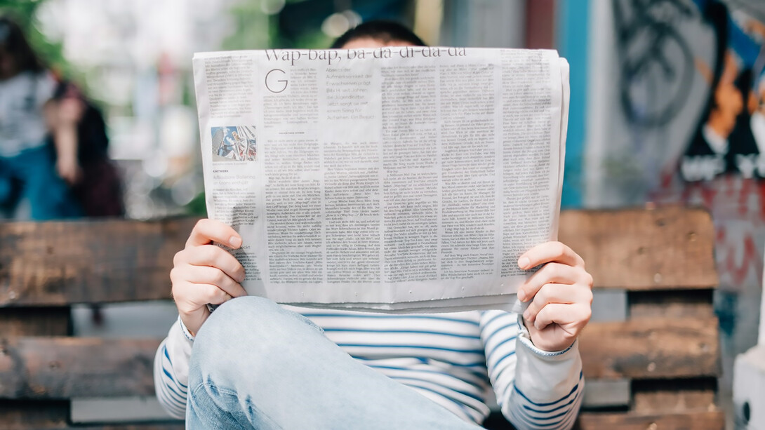 A man sitting on a bench, reading a newspaper