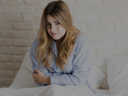 Woman in soft pajamas lying in bed, coping with menstrual cramps and discomfort during her period