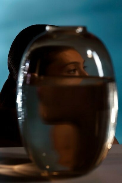 A woman holding a vase partially obscures her face, creating a mysterious and artistic composition, with soft natural light highlighting the delicate details of both the vase and her features