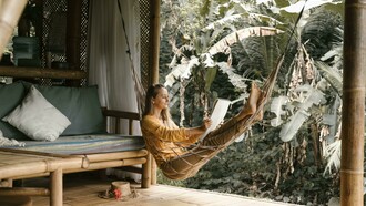 A woman sitting on a hammock, holding a sketchbook during a quiet afternoon