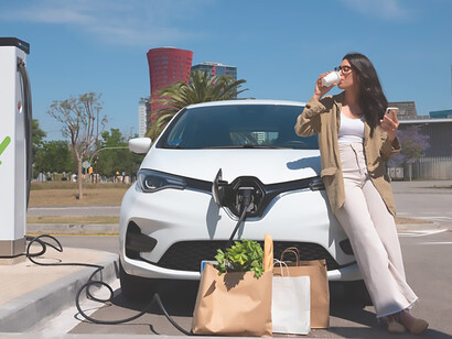 Radiate joy with a smiling woman savoring coffee while patiently awaiting her car to charge, showcasing eco-friendly travel and sustainable lifestyle choices in this vibrant scene