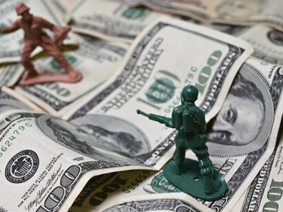 Lifesize classic toy soldier in action, firing at an enemy amidst a dramatic scene of dollar bills, illustrating the juxtaposition of childhood play and the grim realities of warfare