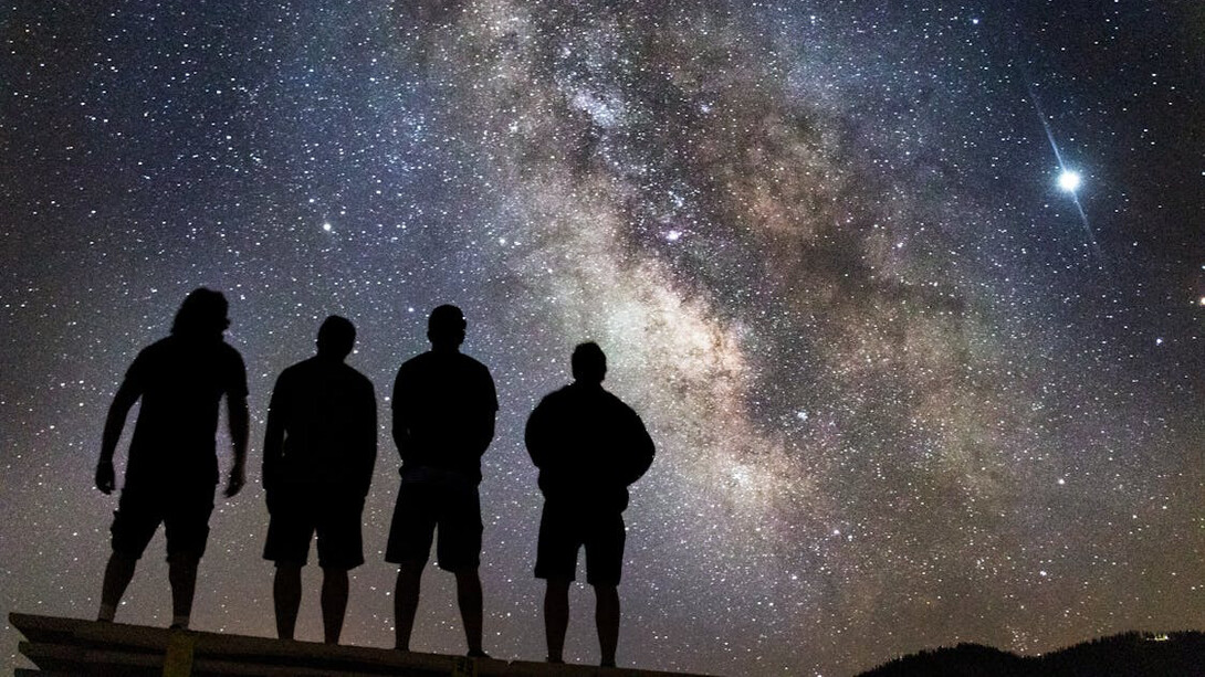 Beneath a blanket of stars, a group gazes skyward, finding solace in the vastness of the cosmos, where individual plans fade into the brilliance of universal mysteries