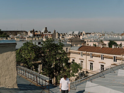 Above the city's skyline, amidst a sea of rooftops under clear blue skies, he reflects on restless nights haunted by the echoes of the city's melodies