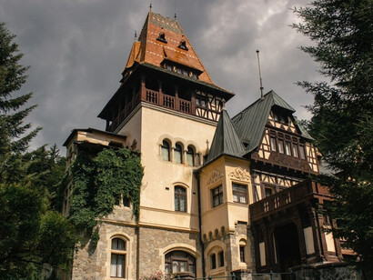 Discover a picturesque scene featuring a charming building adorned with a balcony, alongside the captivating Castelul Pelișor, all set against the scenic backdrop of Sinaia, Romania