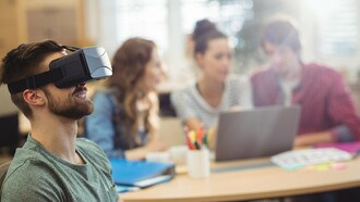 Um homem utiliza um equipamento de realidade virtual enquanto outras pessoas trabalham ao fundo. As novas tecnologias transformam o ambiente profissional, mas não eliminam a importância das relações humanas nas organizações. A evolução tecnológica avança rapidamente, desafiando profissionais e empresas a se adaptarem continuamente. O desafio permanece o mesmo: equilibrar inovação, desenvolvimento humano e construção de carreiras com propósito