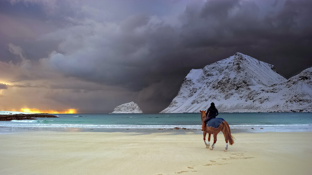 A woman rides a horse near the beach as a storm comes in