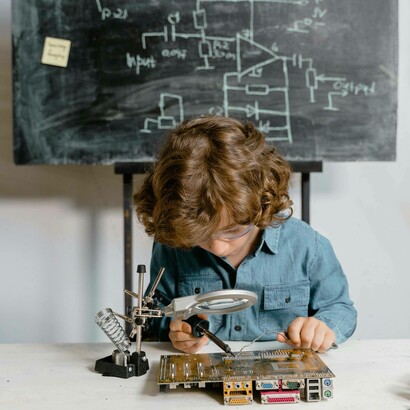 Bambino con lente di ingrandimento impegnato a studiare un circuito