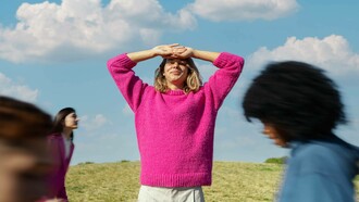 Donna all'aperto che si protegge gli occhi dal sole sorridendo: "Il giusto mix tra eyeliner e olio motore è la metafora di una donna che sa muoversi tra autonomia e connessione, indipendenza e interdipendenza, femminilità e prontezza"