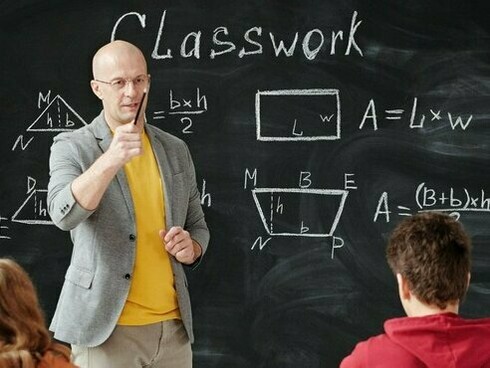 A teacher standing before a classroom, asking questions and interacting with his students